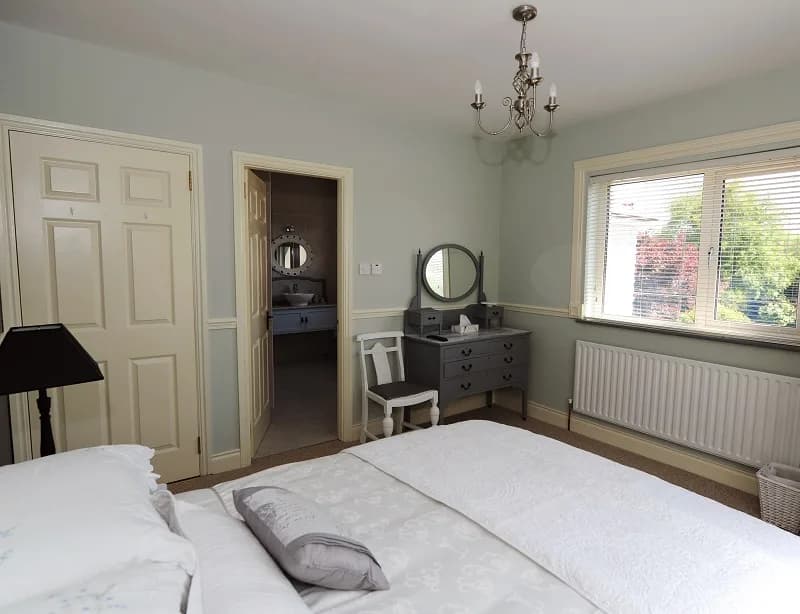 A guest room in soft green, with the ensuite door open onto the washbasin