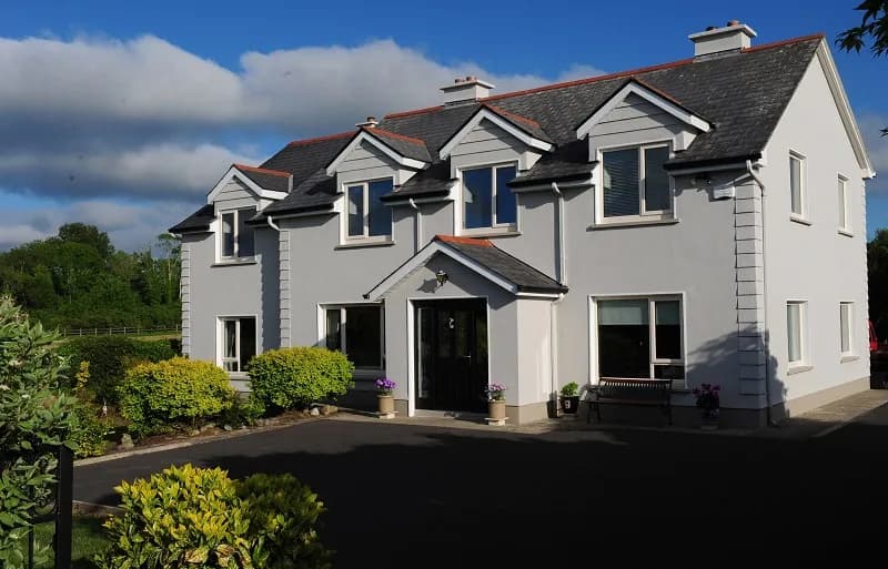 The front of Kingfisher Lodge, a white two storey house with dormer windows and a slate roof, in evening light
