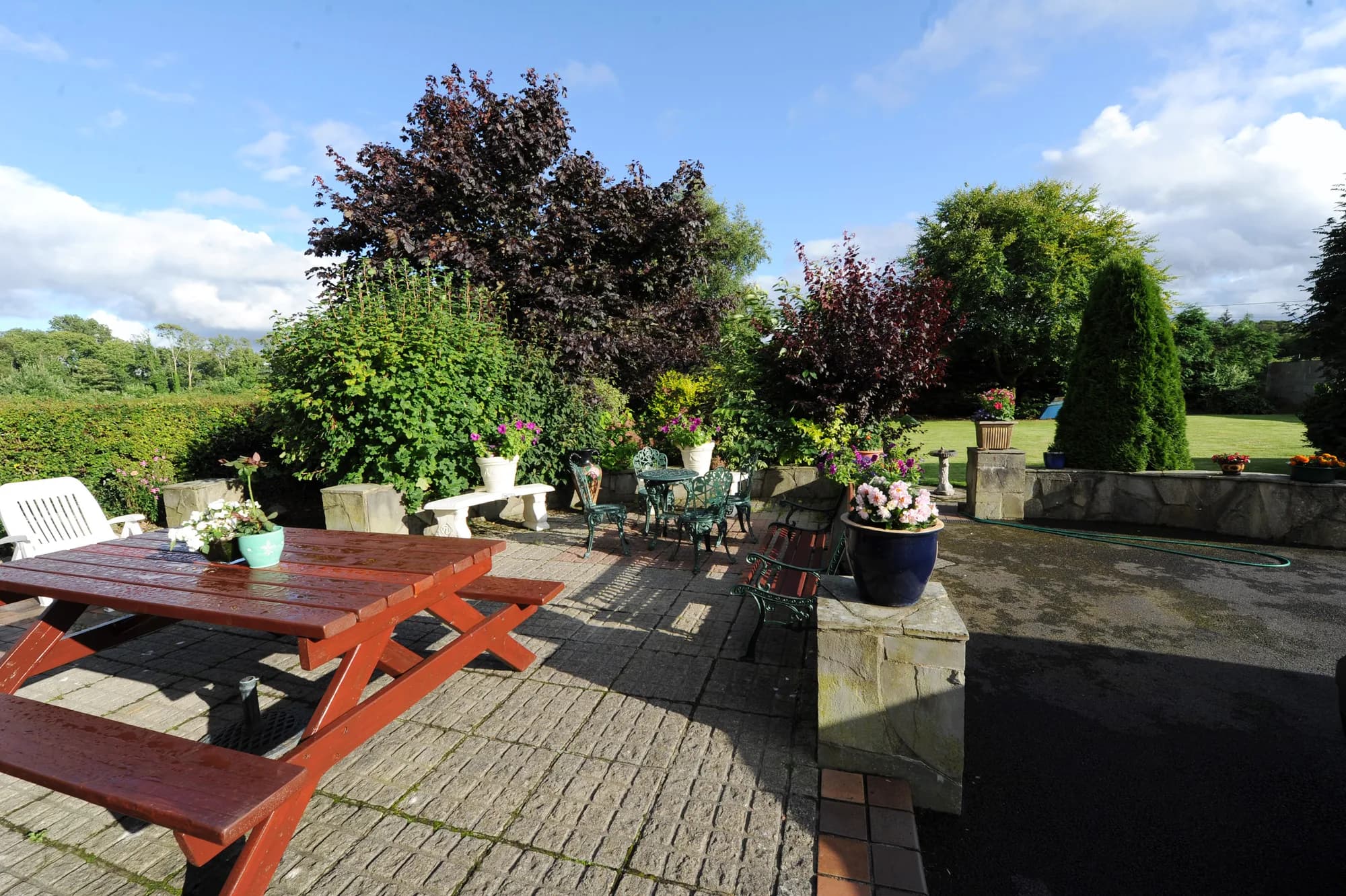 The paved patio with a picnic table and cast iron garden furniture, surrounded by planted borders and lawn